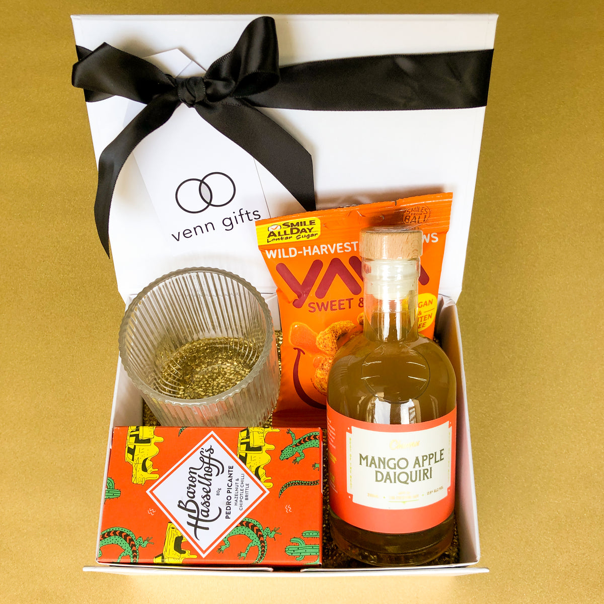 Daquiri, glass, nuts and baron hasselhoff's brittle displayed in a white giftbox with black ribbon against a gold background by Venn Gifts