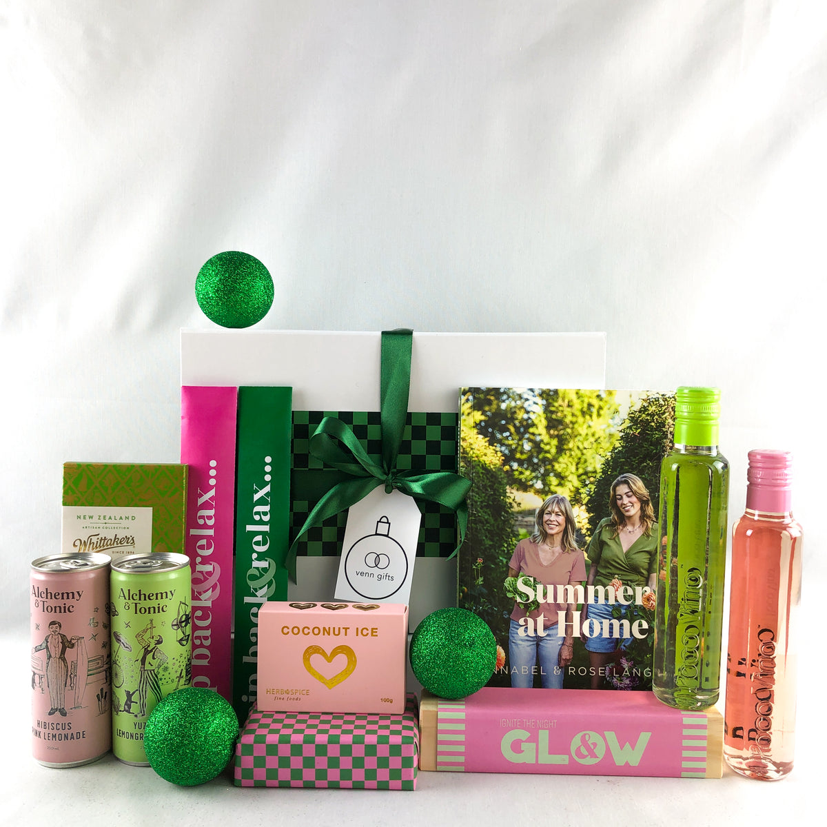 A curated gift box arrangement on a white studio background, featuring a white gift box tied with a green ribbon including annabel langbein recipe book.