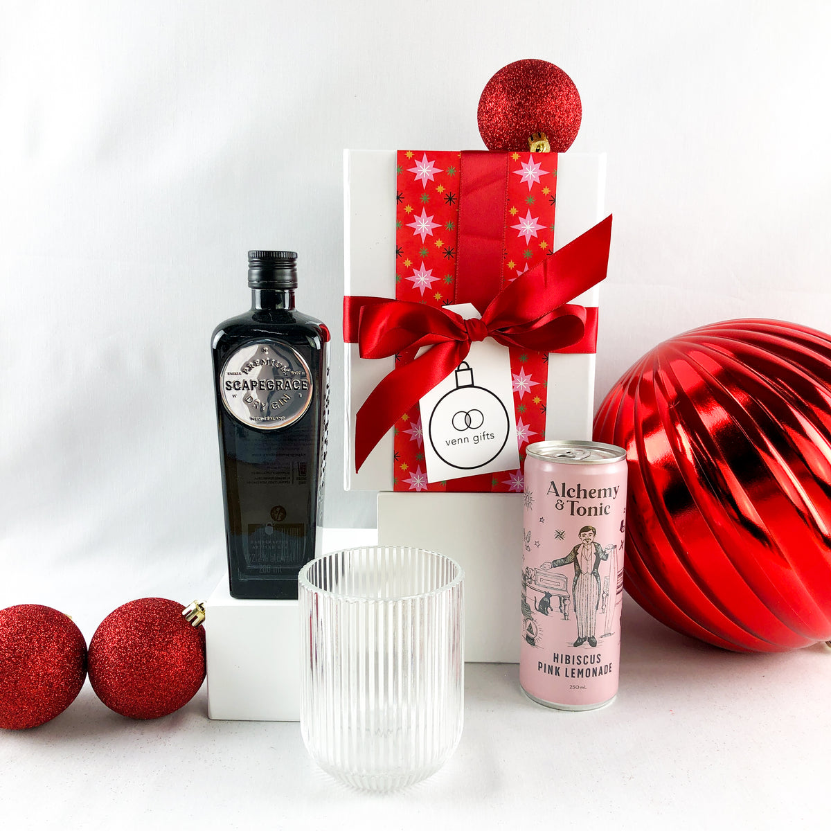 Scapegrace gin, reeded glass and alchemy & tonic hibiscus lemonade presented in front of a white gift box with a red ribbon by Venn Gifts.