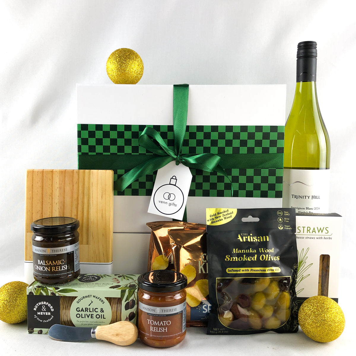 Snacks, olives, wine, chopping boards arranged in front of a white giftbox with green ribbon by Venn Gifts.
