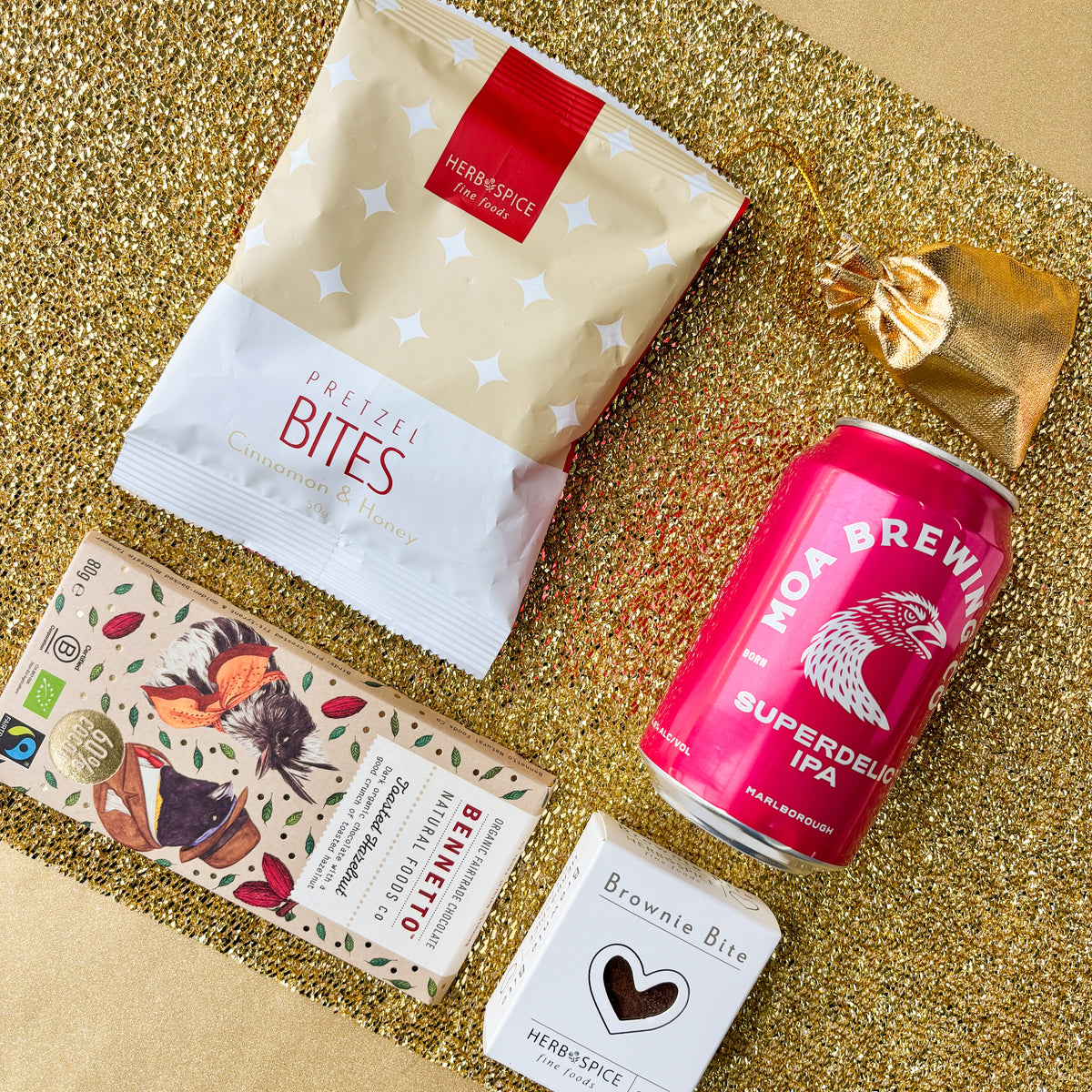 product flatlay against a gold background. Containing pretzel bite, bennetto chocolate moa brewing ipa, brownie bite, gold drawstring pouch filled with lollies from Venn Gifts.