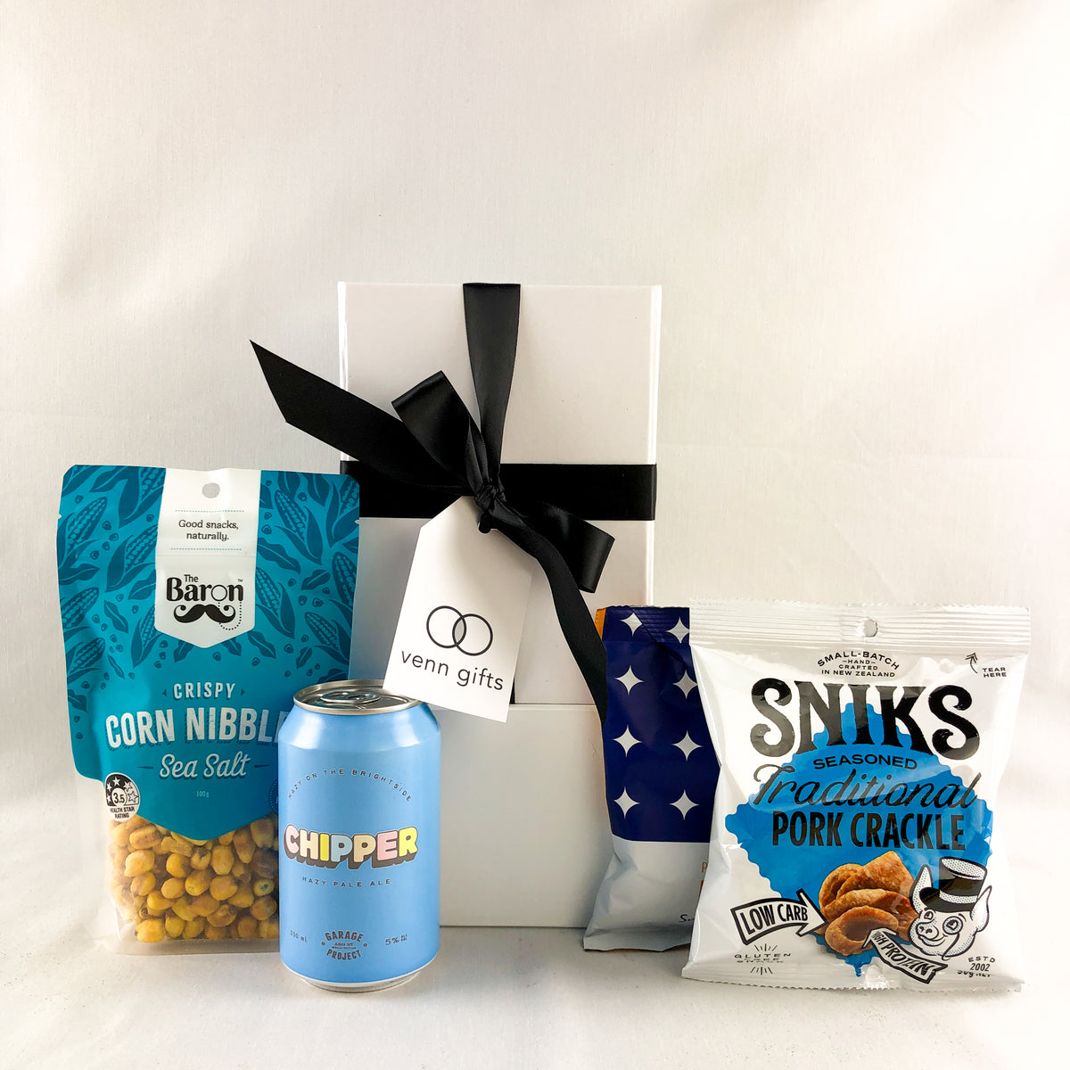 Chipper beer and snacks in front of a white giftbox with black ribbon by Venn Gifts.