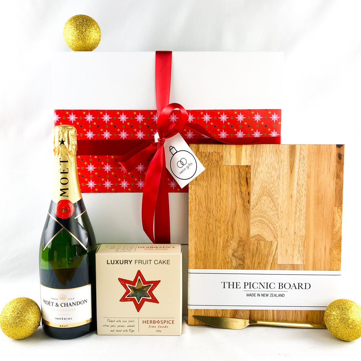 moet, luxury fruitcake a chopping board & gold knife in front of a white giftbox with a red ribbon by Venn Gifts.