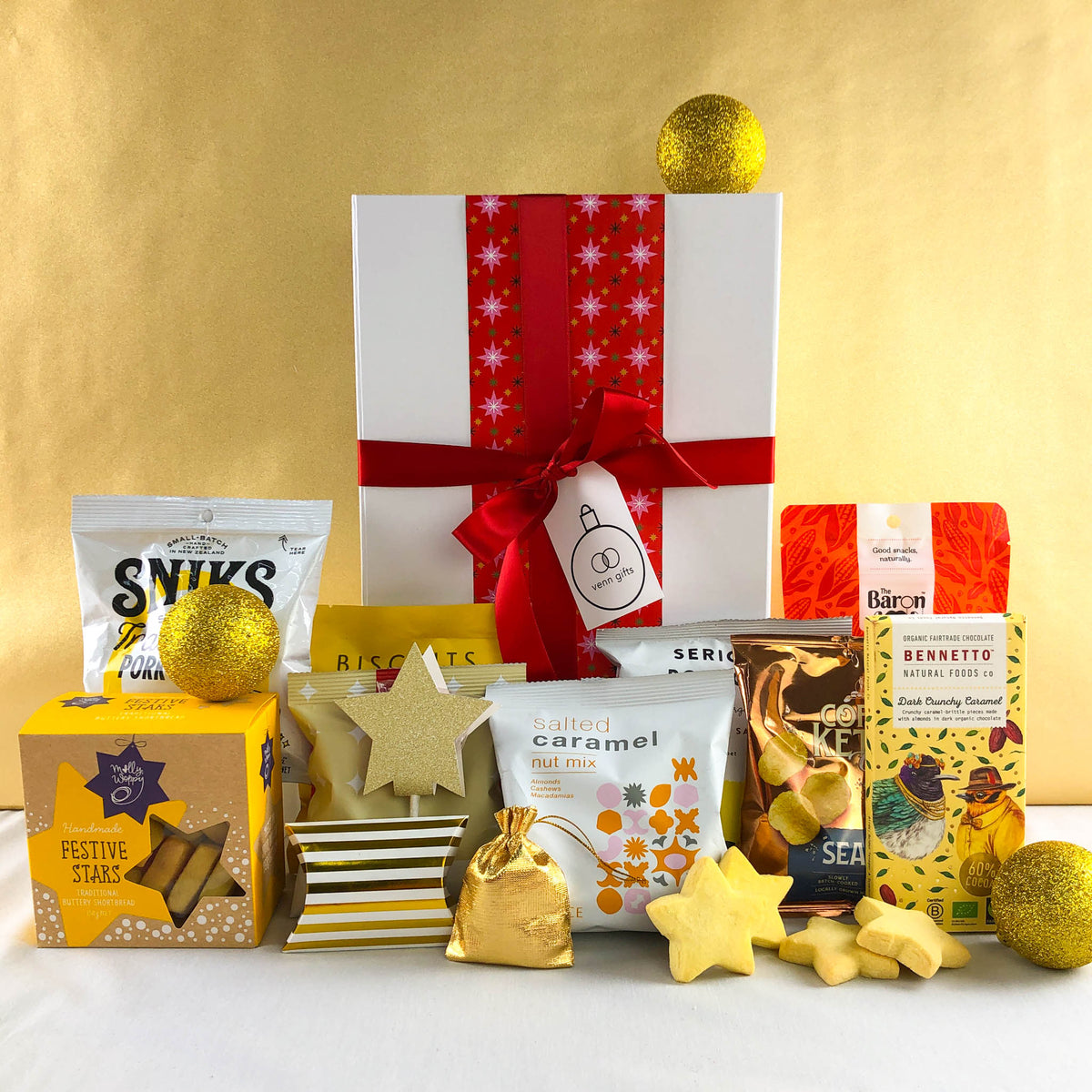White gift box with red ribbon against a gold background surrounded by snacks for a team, corporate or family gathering by Venn Gifts.