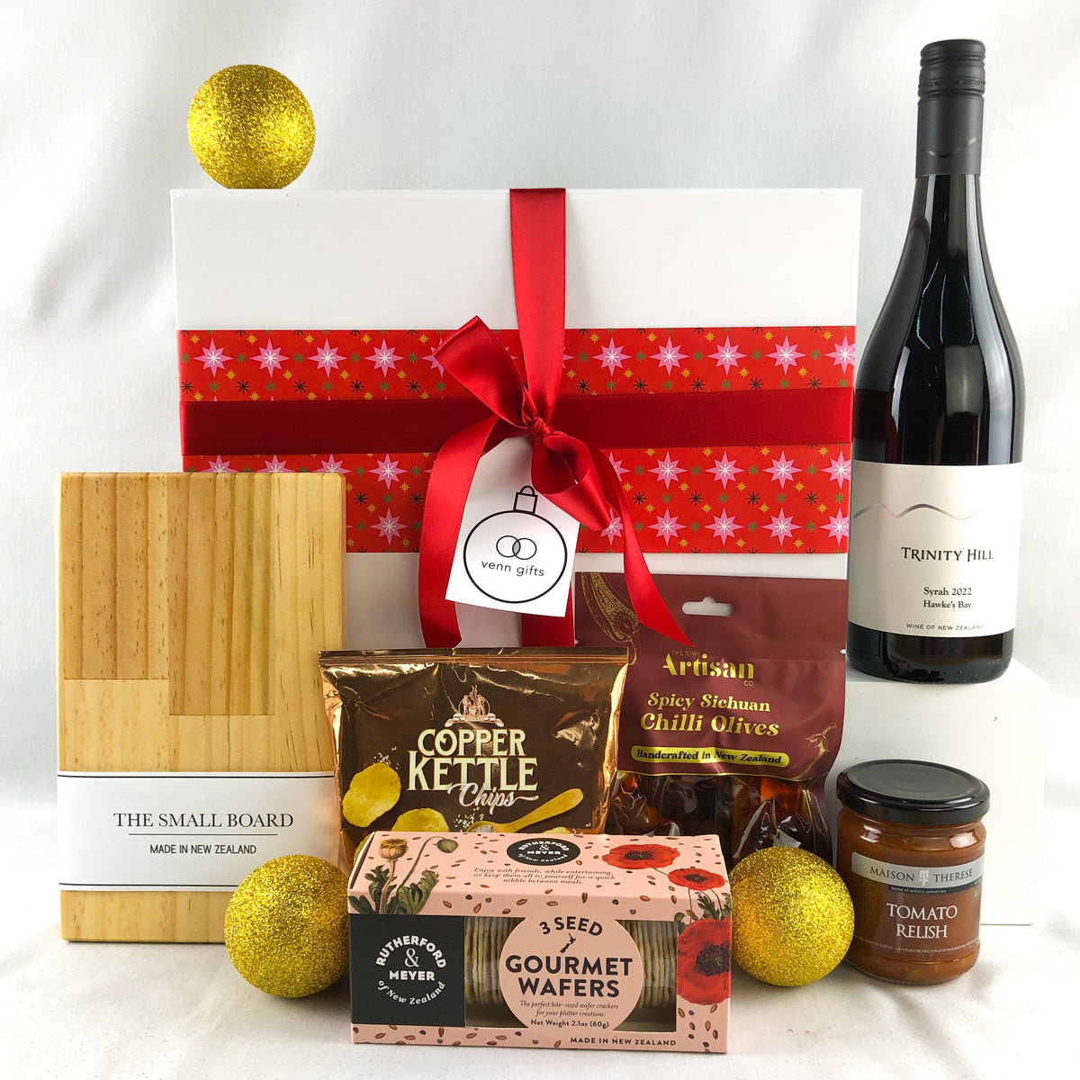 trinity hill wine, snacks, crackers, relsish and small chopping board and olives set against a white gift box with red ribbon from Venn Gifts.