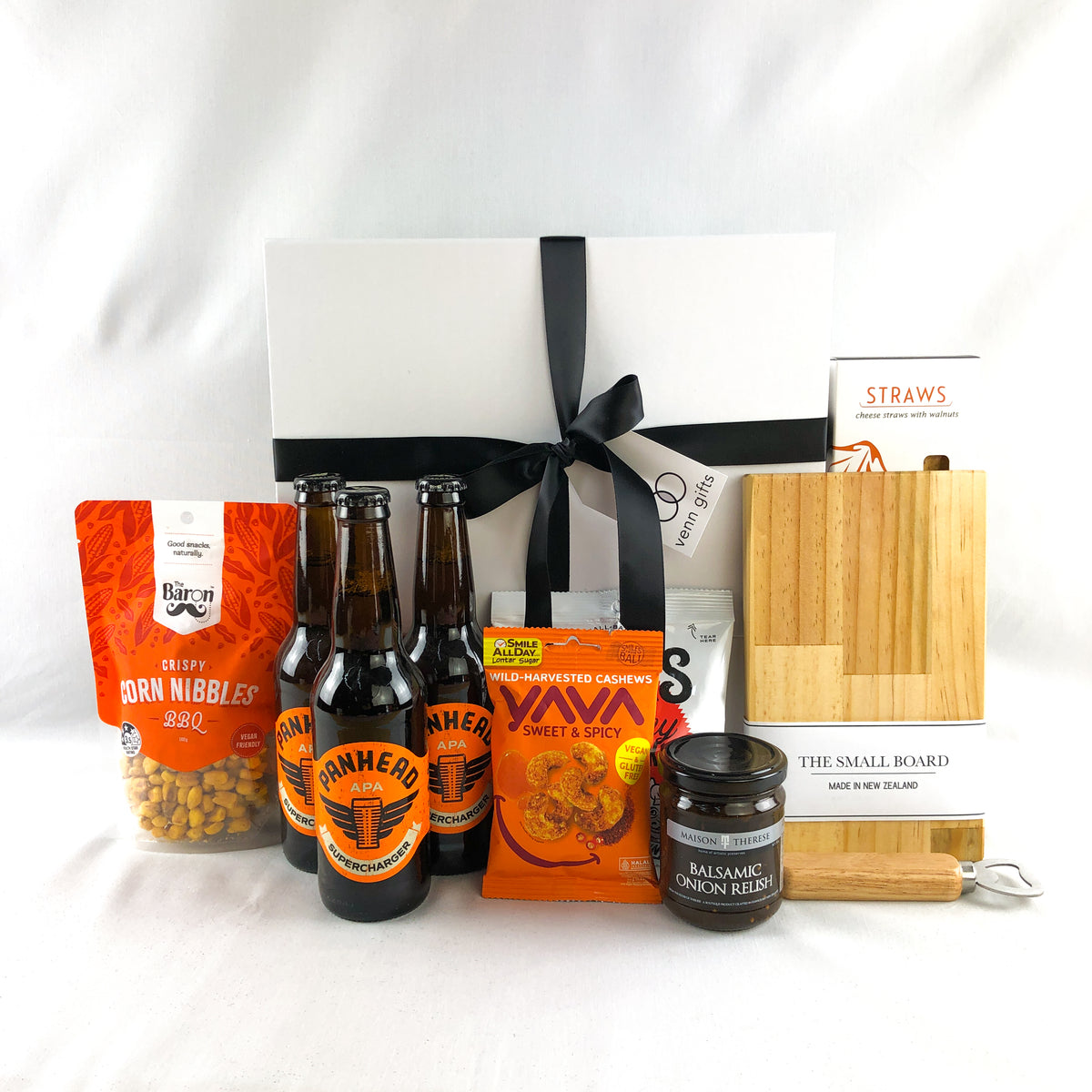 snacks, beers and treats in front of a white giftbox with red ribbon by Venn Gifts